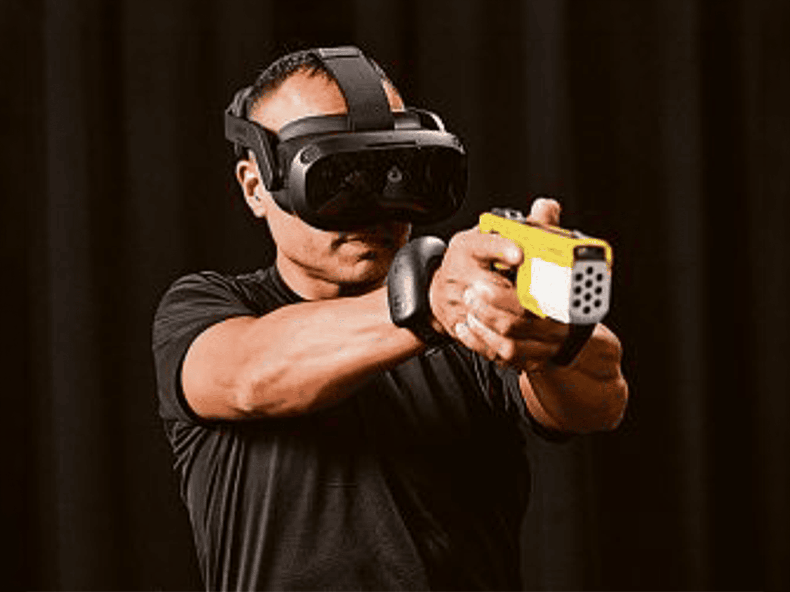 Person wearing VR headset aiming a yellow toy gun in a dark room.