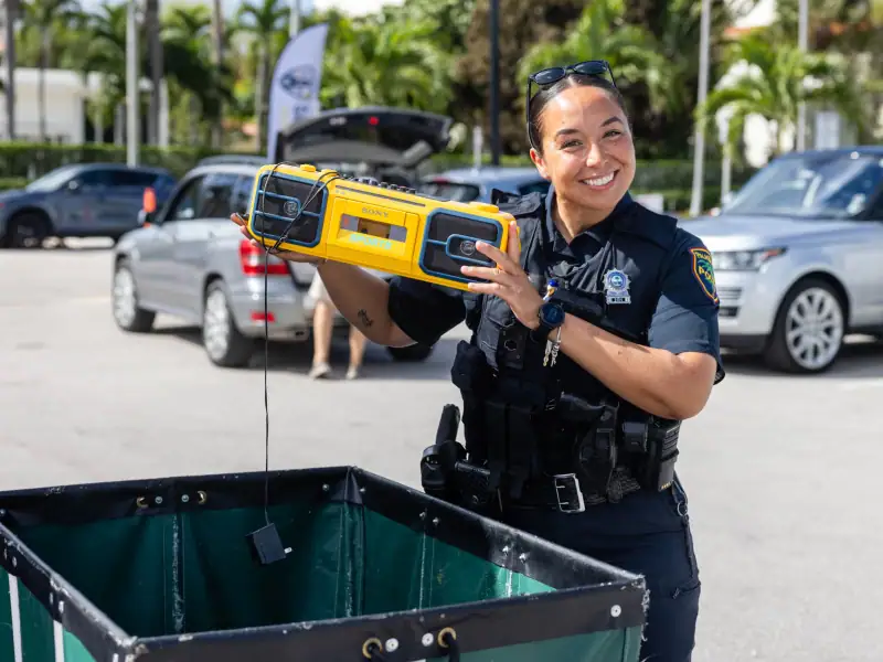 Police officer smiling with a portable device at Palm Beach event.