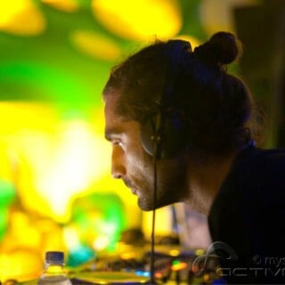 Arjuna DJ performing at Partybody, focused on mixing music with vibrant lighting in the background.