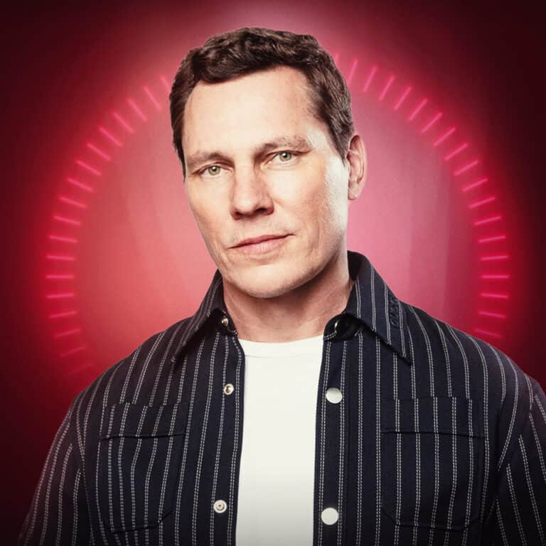 A portrait of a confident man with a serious expression, set against a vibrant red background with c.