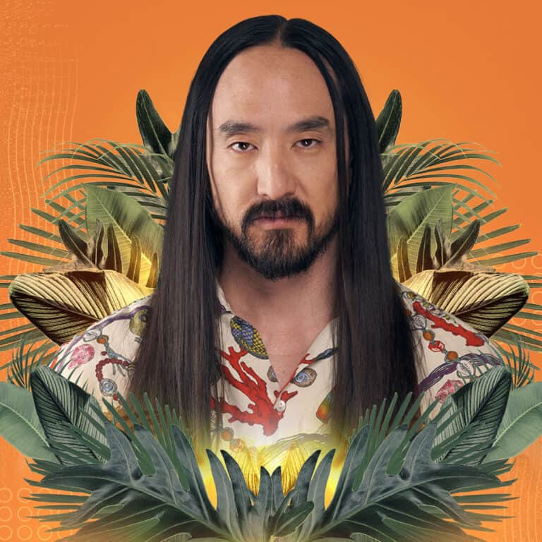 A man with long dark hair and a beard, wearing a colorful floral shirt, surrounded by lush tropical.
