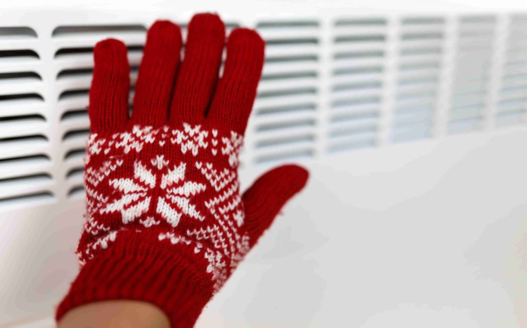 Red and white knitted glove touching a white radiator