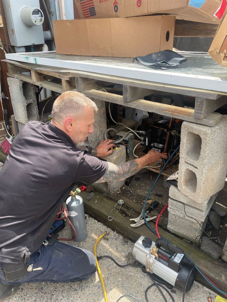 Man working on outdoor refrigeration unit with tools and equipment.