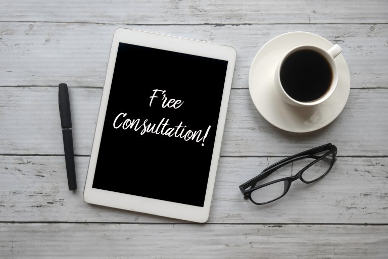 Tablet with 'Free Consultation!' text, pen, coffee, and glasses on a wooden table.