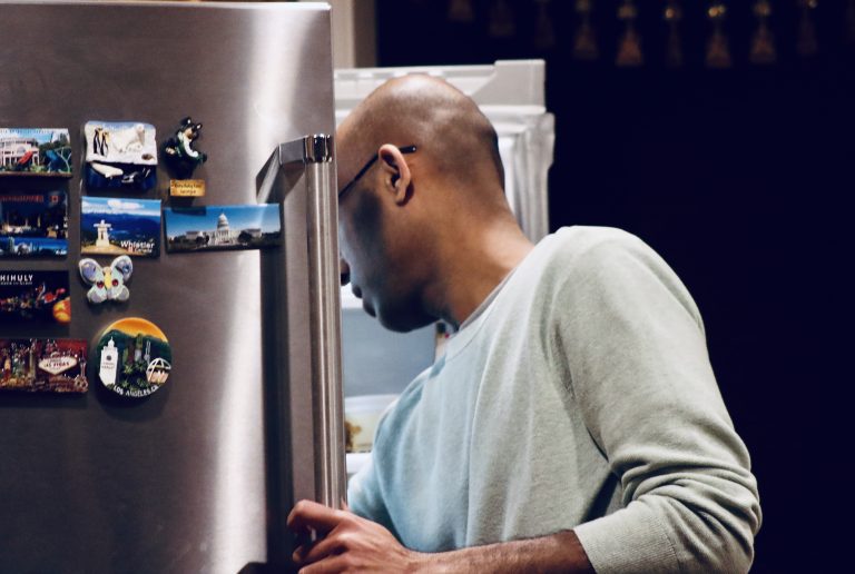 Man looking into a stainless steel refrigerator adorned with magnets.