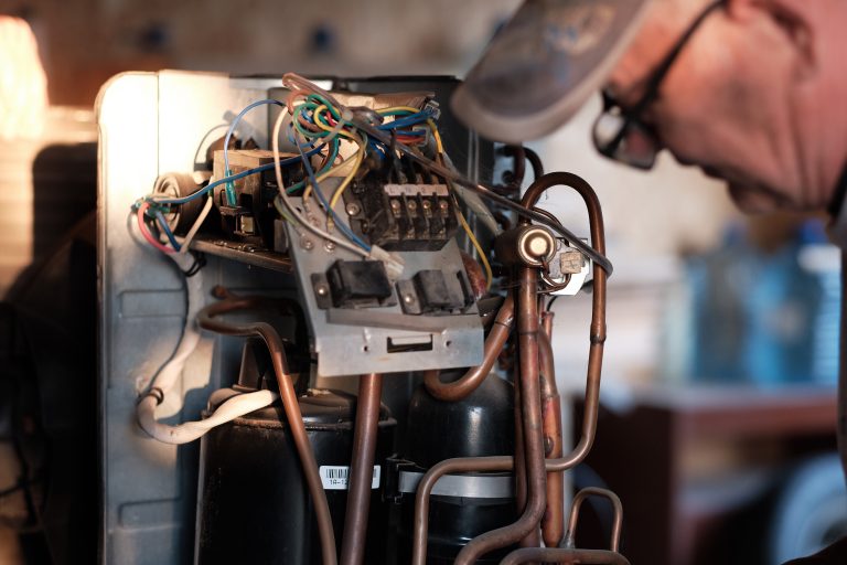 Person working on the exposed wiring and copper pipes of an appliance.