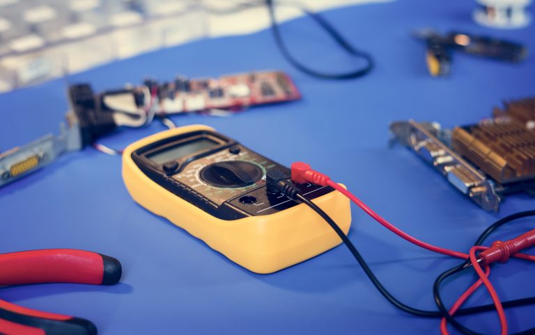 Close-up of a yellow multimeter with red and black probes on a blue surface.