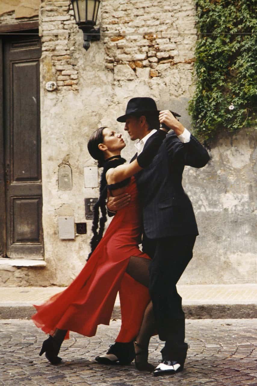 Couple dancing passionately on cobblestone street with rustic stone wall background.