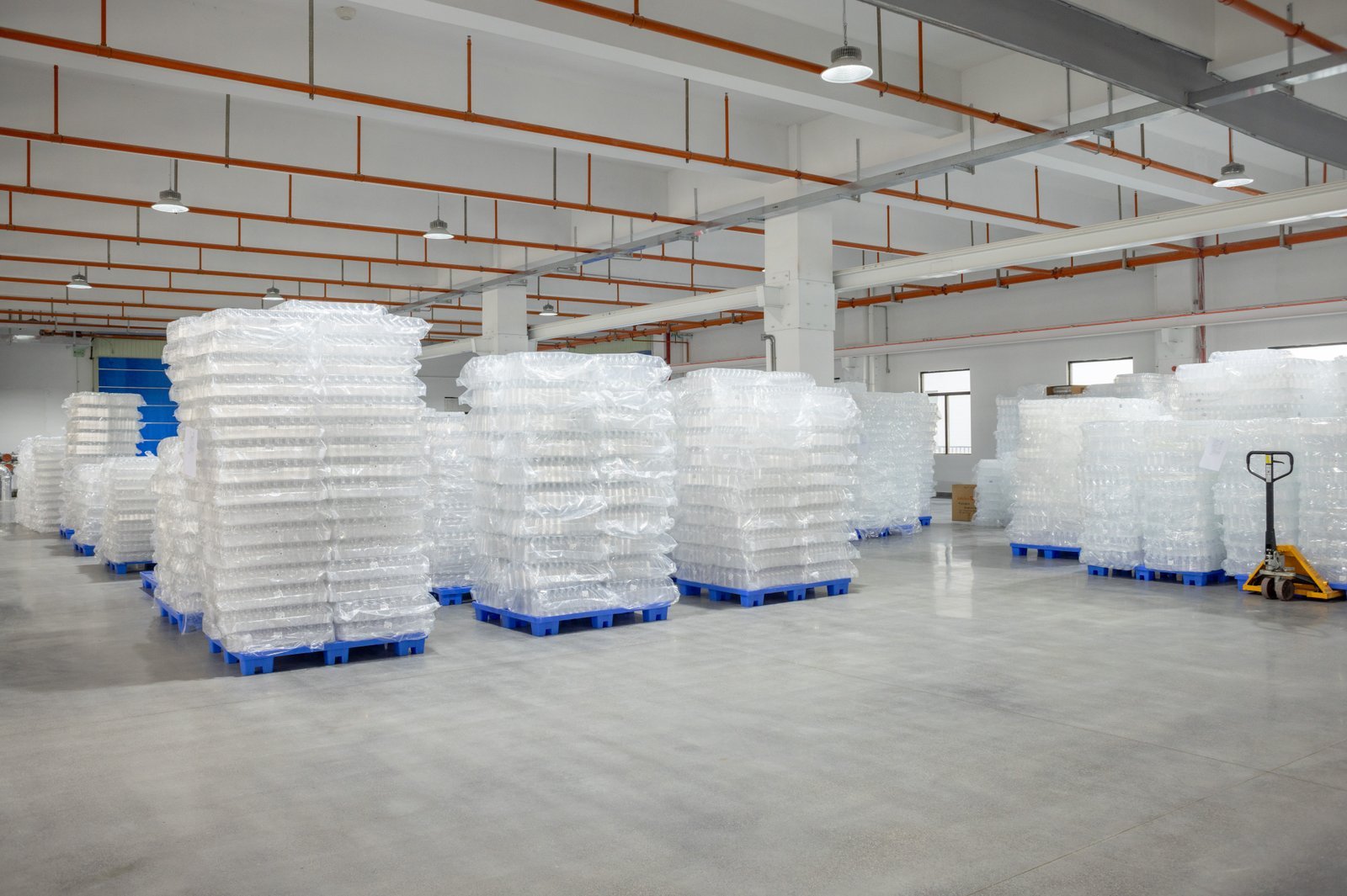 Warehouse with stacked plastic containers on pallets in a manufacturing facility.