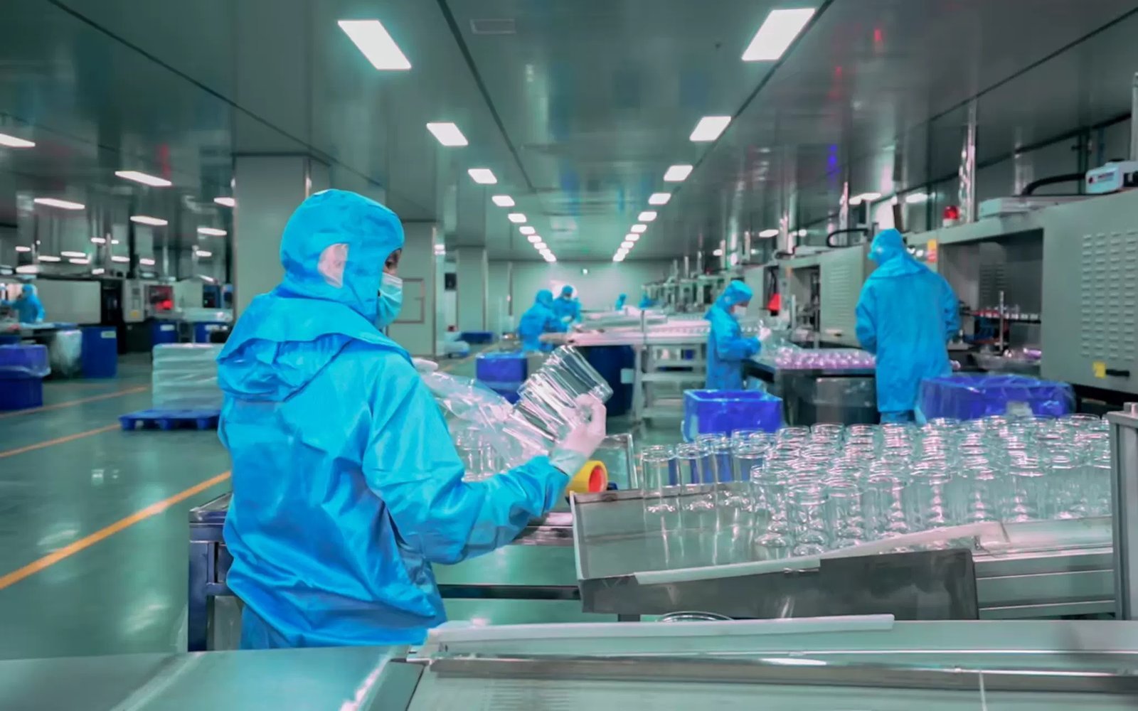 Cleanroom workers inspecting glass bottles in manufacturing facility.