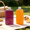 Purple and orange plastic bottles on a picnic table outdoors, with a basket and snacks in the backgr.