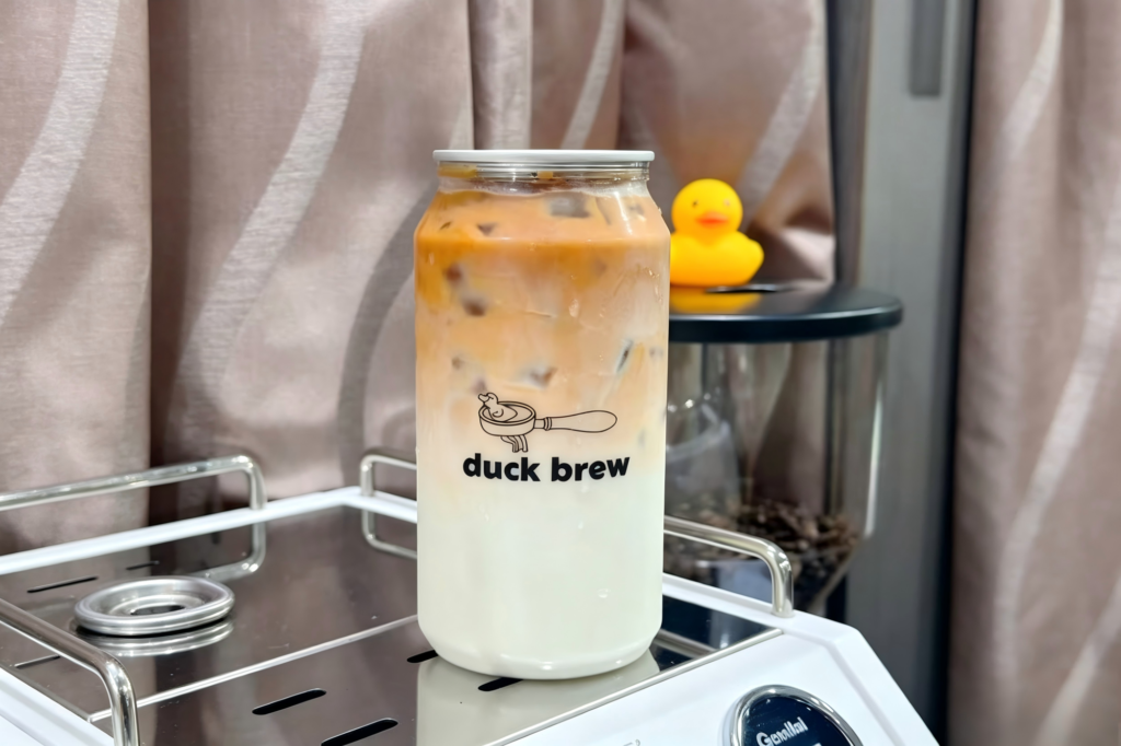 Glass jar with iced coffee and milk, branded 'duck brew' on the label.