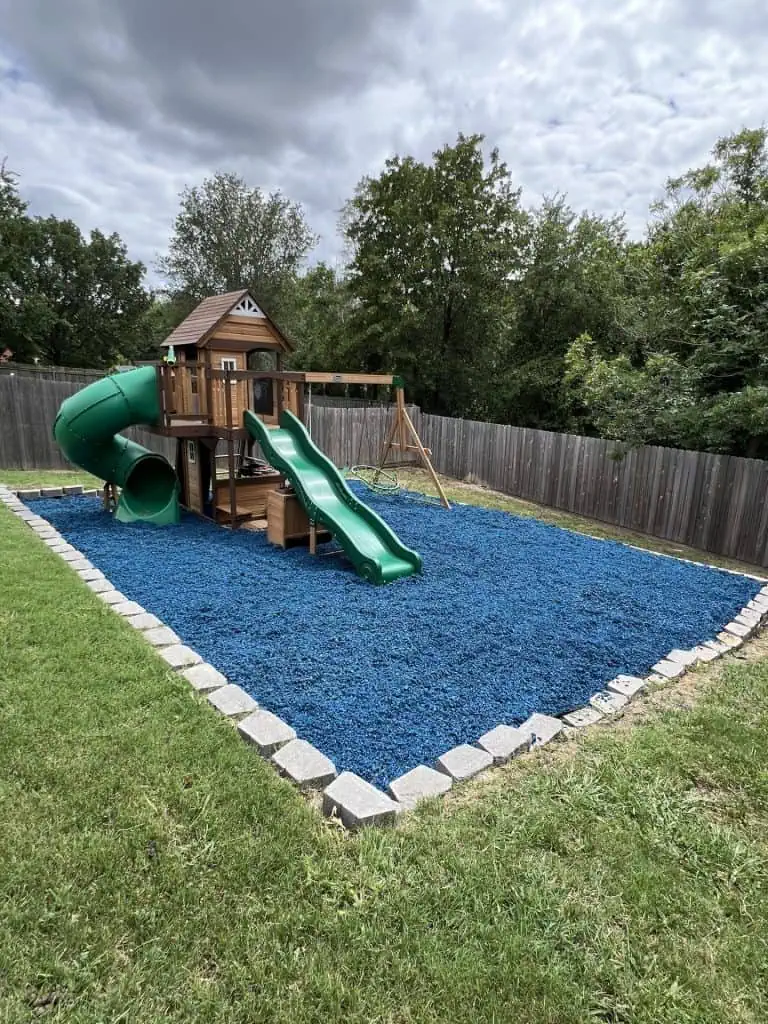 Wooden playset in backyard in large, blue mulch pit.
