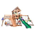 Children playing on a large wooden outdoor playset with slide and swings.