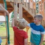 Children playing on a wooden outdoor playset in a grassy yard.