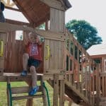 Children playing on a wooden outdoor playset in a backyard.
