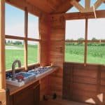Wooden playhouse under construction with open windows and outdoor scenery.