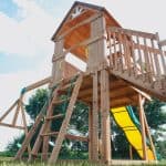Wooden outdoor playset with slide and climbing ladder for kids in backyard.