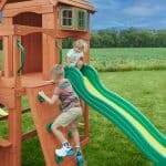 Children playing on a wooden outdoor playset with slide in a grassy field.