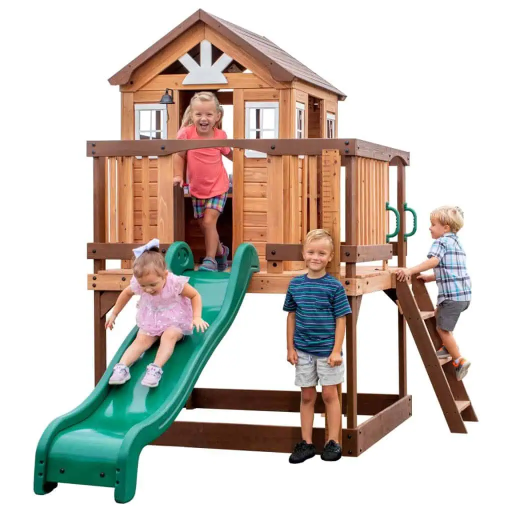 Children playing on a wooden playhouse with slide and climbing ladder.