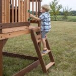 Young boy climbing wooden playhouse stairs outdoors in Texas.