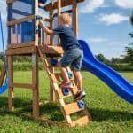 Child climbing wooden playset with slide in backyard.