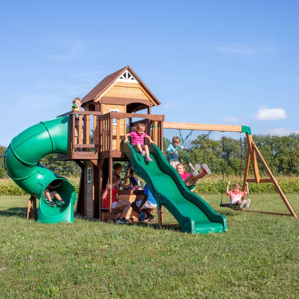 Children playing on Cedar Cove swing set with slides and swings in Texas backyard.