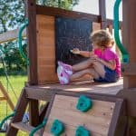 Young girl drawing on chalkboard at outdoor playset in Texas.