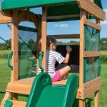 Child drawing on chalkboard in outdoor playset with slide.