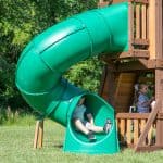 Children playing on a green outdoor slide attached to a wooden playset.