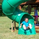 Children playing on a green spiral tube slide at a playground in Texas.