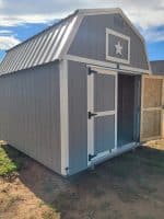 Gray 10×12 lofted barn shed with a small front porch overhang and white trim in an outdoor display area.