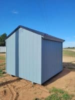 The back side view of a light blue wooden storage shed with a dark gray gabled roof