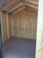 The unfinished interior of a wooden storage shed showing OSB walls and exposed timber framing.
