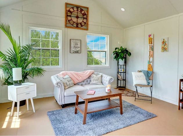 Stylish painted wood shed repurposed as a cozy backyard workspace with natural light and decor.