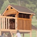 A low-angle shot shows a wooden playhouse and a small girl climbing a ladder. The playhouse has a brown roof, wood-paneled walls, and a small window. It is built on a raised platform, part of a larger playset, with a wooden railing in the foreground. The girl, seen from behind, wears a light purple top and is ascending a ladder made of wooden rungs. In the background, out-of-focus trees and green foliage suggest an outdoor setting. The image has a light, natural feel.