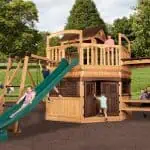 Titan Treehouse XL 13 swing set with double slides, climbing wall, and upper play fort in backyard setting.