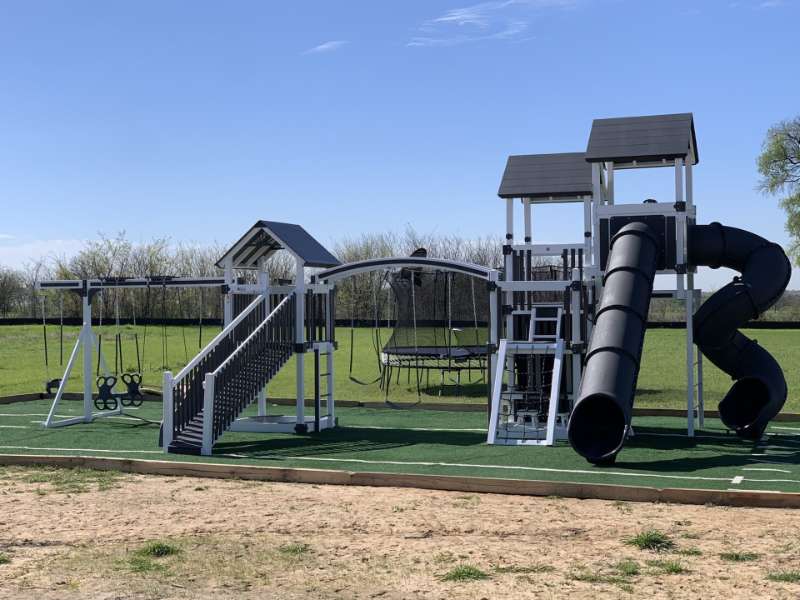 Kids playing on a vinyl playground set with slide and swings in a grassy backyard.