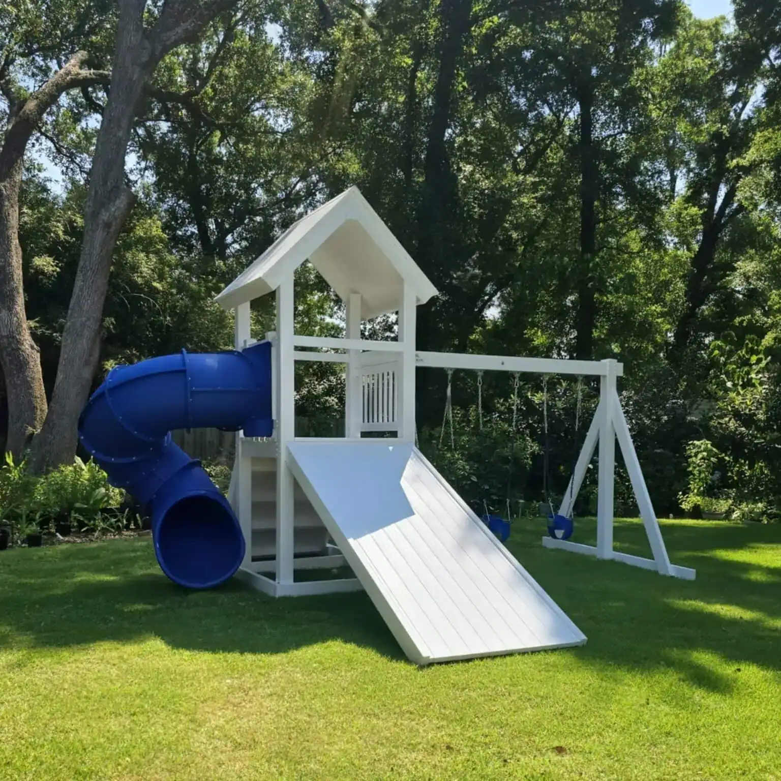 White vinyl playset with a roofed tower, attached slide, and side climbing elements in a green outdoor yard.