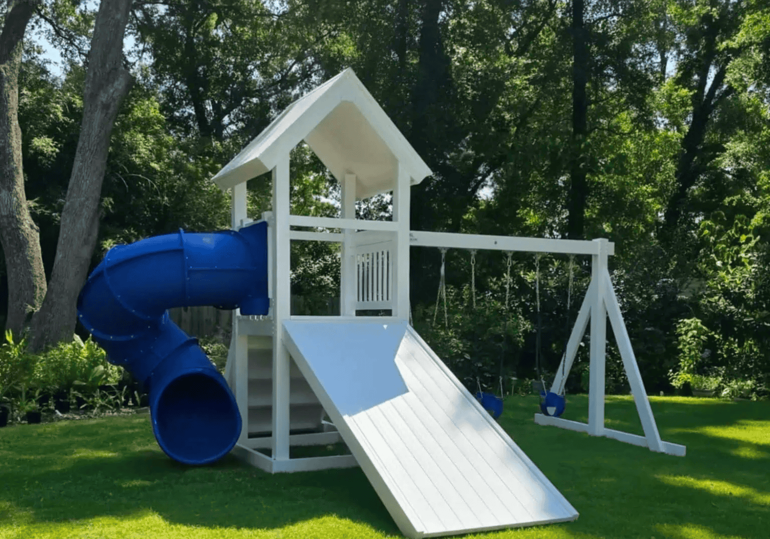 White and green vinyl playset with a central tower and a straight slide extending to the grass.