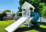 White vinyl playset with a peaked roof, ladder access, and a green slide in a backyard setting.