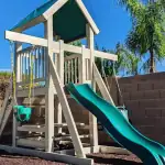 White and teal vinyl playset with a tower, green slide, and climbing structure.