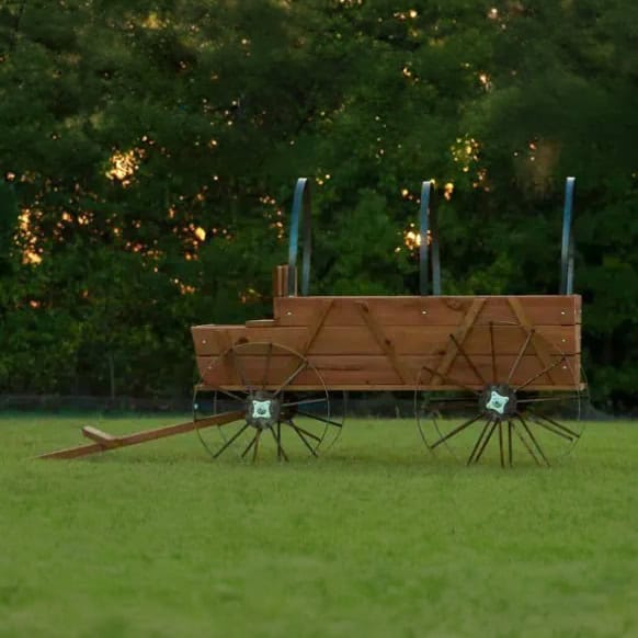 Rustic wooden wagon with metal wheels on grassy field at sunset.