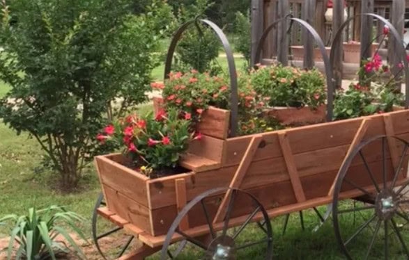 Wooden wagon planter filled with colorful flowers in a garden setting.