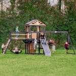 Children enjoying outdoor play on a wooden playground with swings and slide.