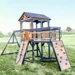 Outdoor wooden playset with slide, climbing wall, and swings for children.