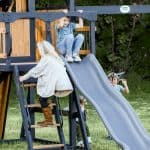 Kids enjoying outdoor play on a wooden playground with slide and swings.
