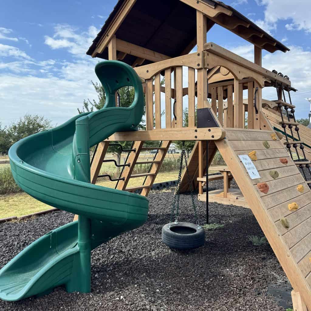 Wooden outdoor playset with slide and climbing wall in North Texas.