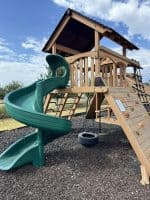 Wooden outdoor playset with slide and climbing wall in North Texas.