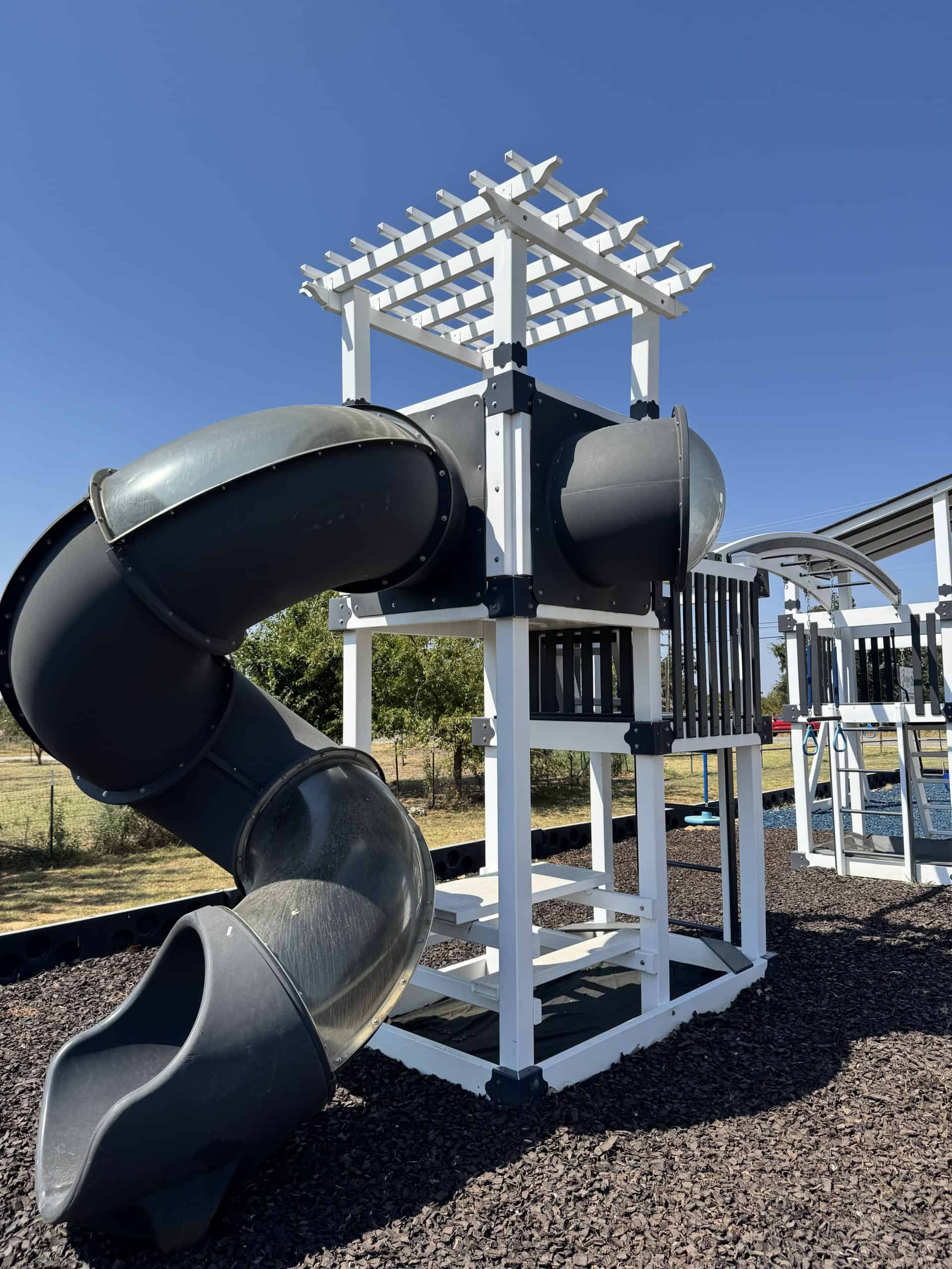 Children's playground with a black tube slide and white wooden structure in Texas.